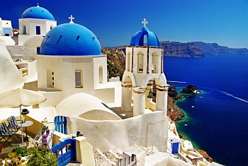 View of white-cubed houses with blue domes backdropped by the blue sea and the caldera view on the Greek island of Santorini