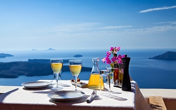 Table of glasses of wine and view of the caldera and the vast blue sea on Santorini island