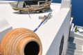 A clay pot and a fishing boat decorating the roof of a white-washed Santorinian house