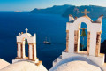 Church bell towers backdropped by the vast blue sea and a sailing ship, Santorini island